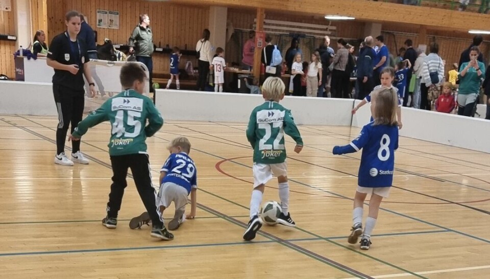 Barn spiller fotballkamp på en liten bane i en gymsal.