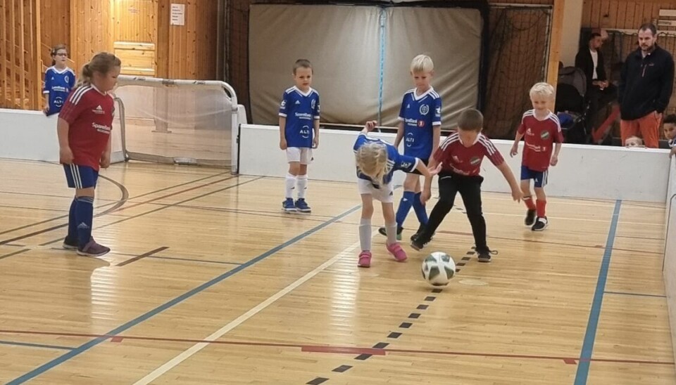 Et blått lag og ett rødt lag. Barn spiller fotballkamp på en liten bane i en gymsal.