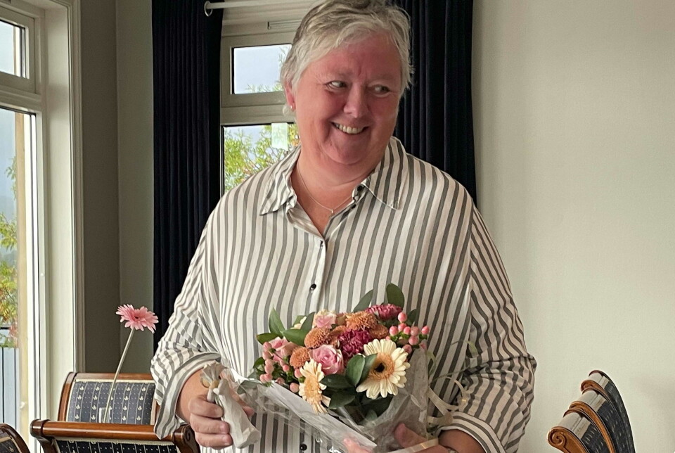 Takk til Marit for allsidig teneste – og for det hyggelege smilet som også pregar dette portrettet av ein populær arbeidskollega. En kvinne smiler og holder blomster