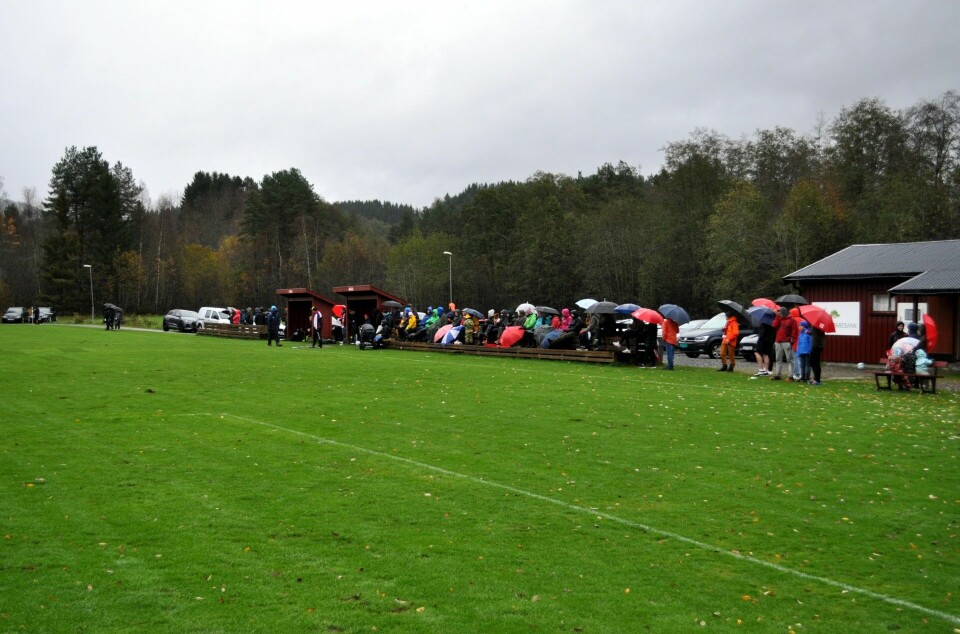 Mange mennesker med paraply ved en fotballbane.