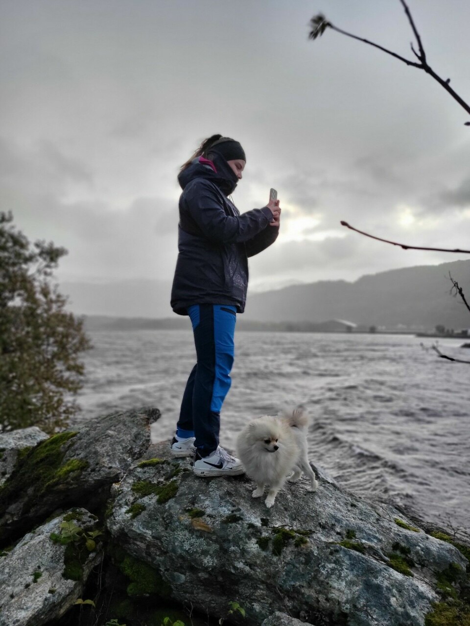 Hund og menneske på en stor stein ved elv/sjø.