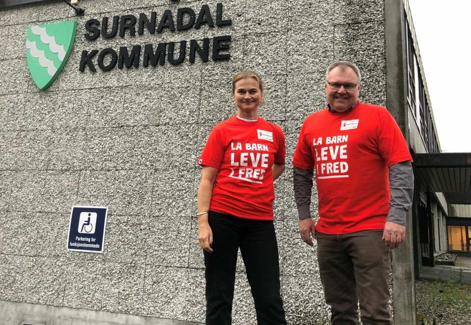 En kbinne og en mann i røde T-skjorter står sammen foran Surnadal Kommune sin bygning.