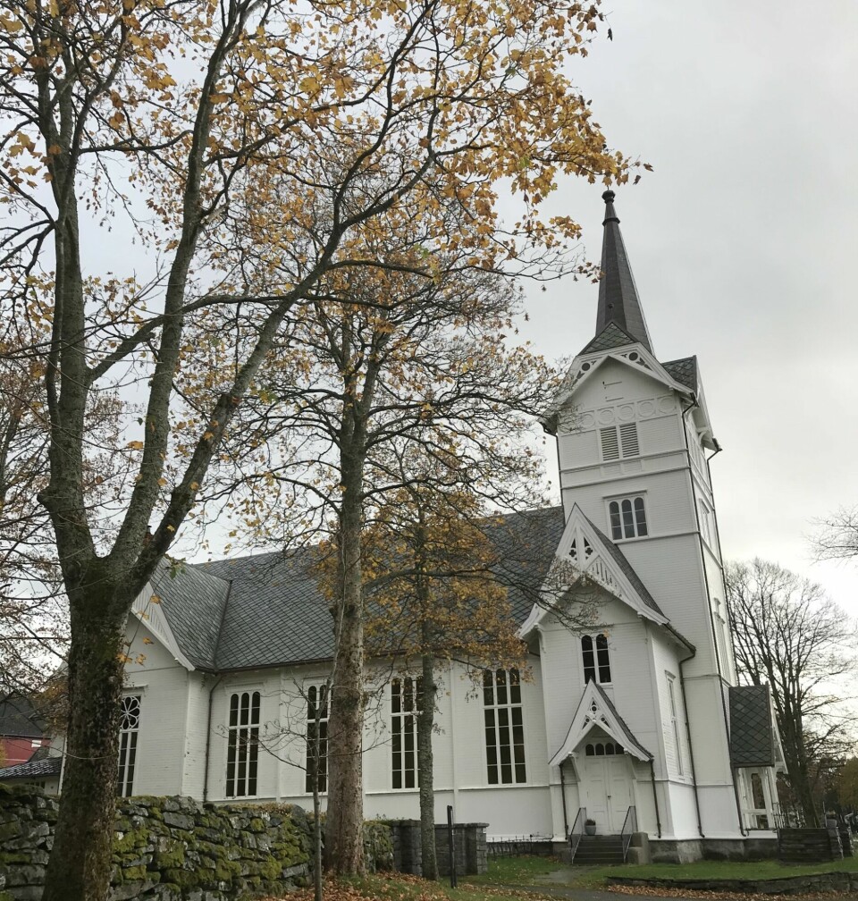 En hvit kirke med trær som mister bladene sine om høsten