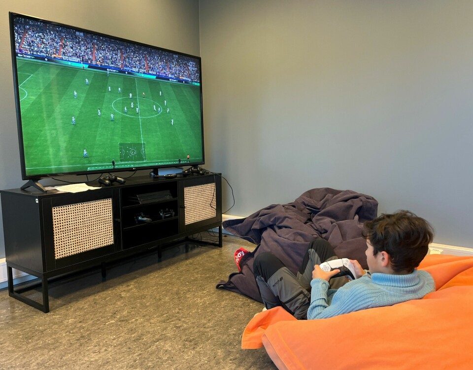 En gutt som sitter i en saccosekk og spiller fotballspill på en stor TV-skjerm