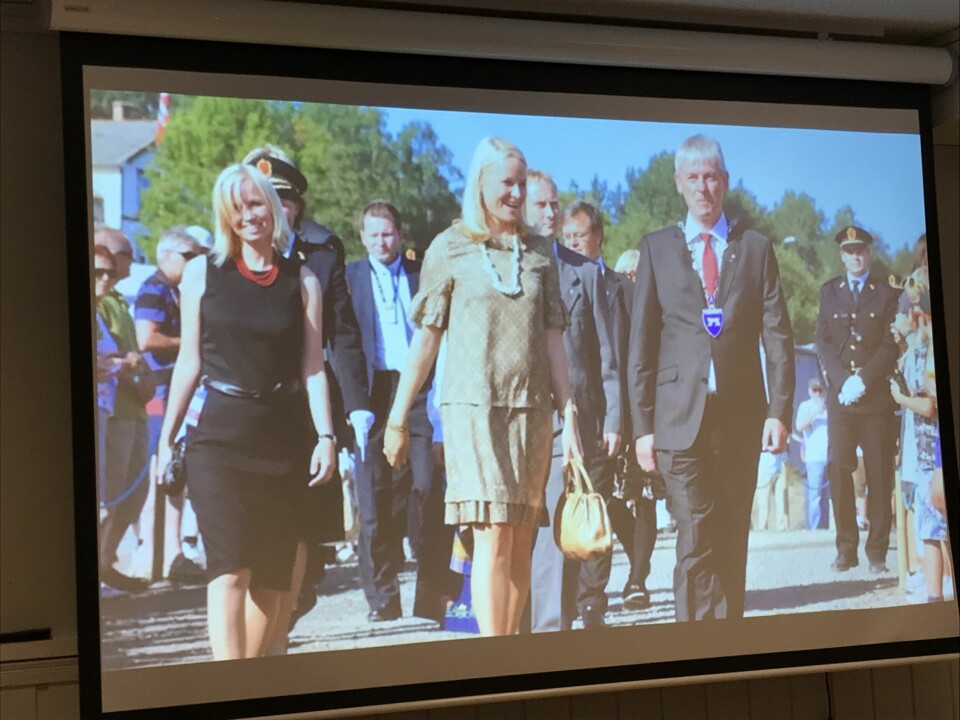 Bilde fra en skjerm hvor to kvinner og en mann går foran en stor samling av andre mennesker bak seg