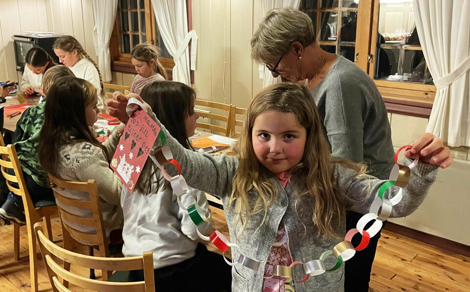 En liten jente holder opp en julelenke i glanspapir med andre barn bak seg
