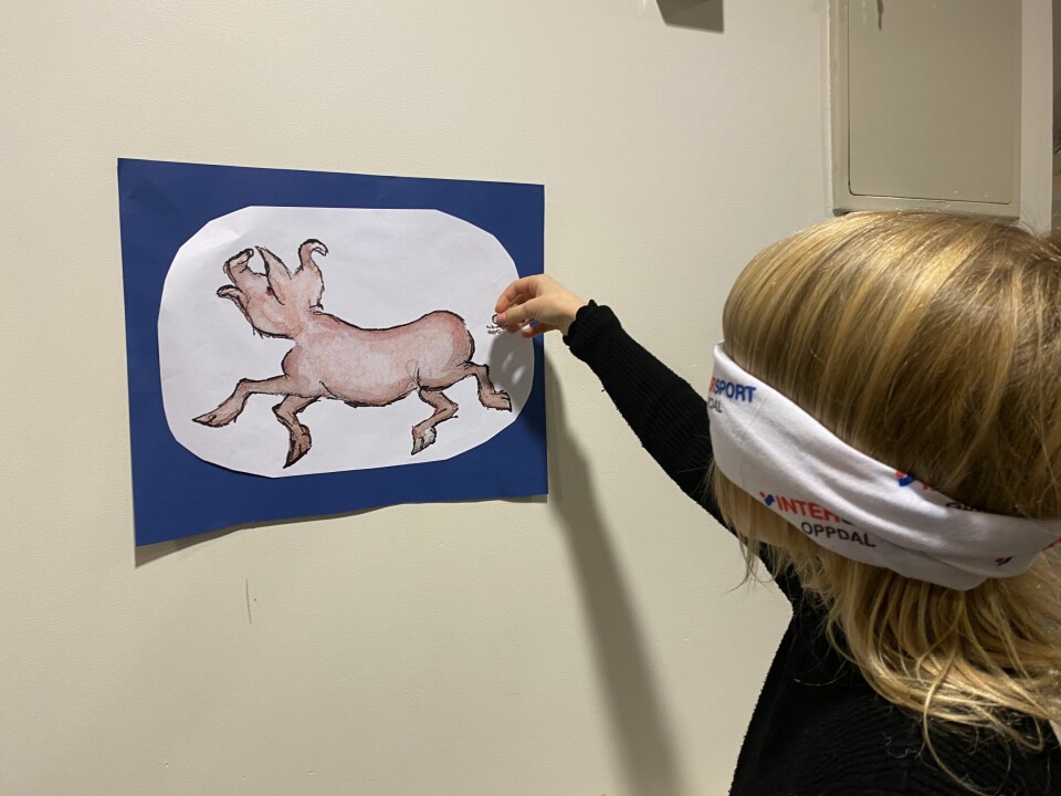 Et barn med bind for øynene som setter på en hale på en tegning av en gris på veggen.
