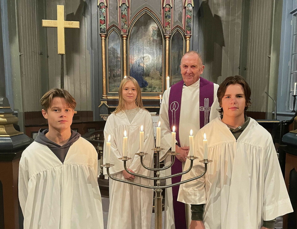 En prest og tre konfirmater i kapper foran alteret i kirka.
