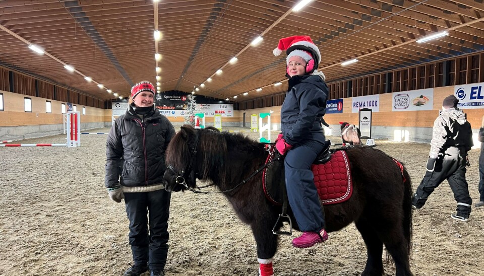 Jente som sitter på hest, og dame som står ved siden av