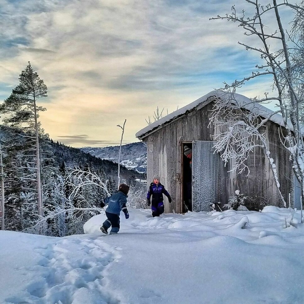 To barn leker i snøen på vei inn i gammelt trebygg.
