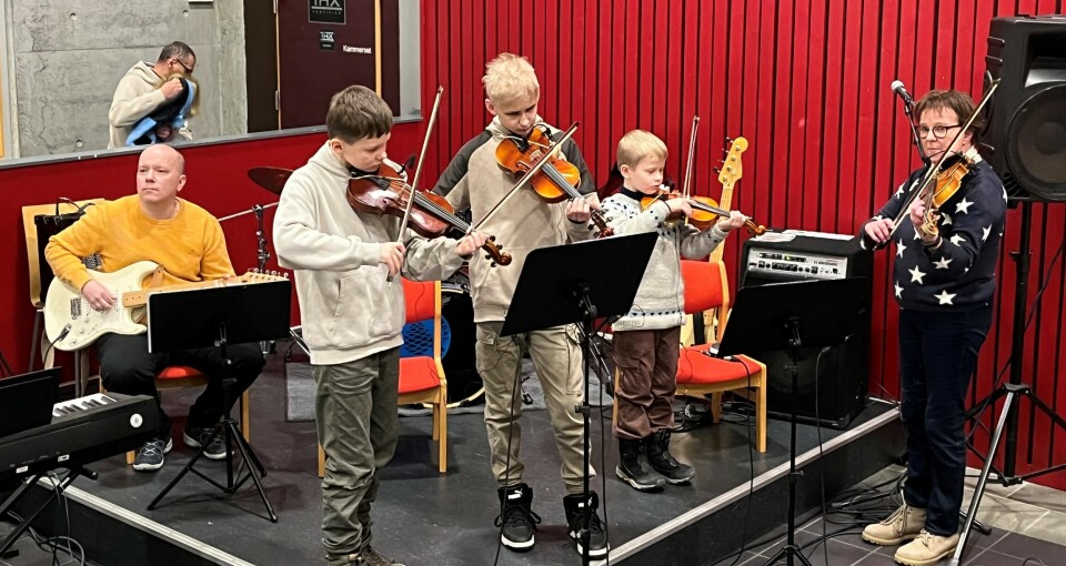 Tre barn og en voksne som spiller fiolin. En voksen spiller gitar.