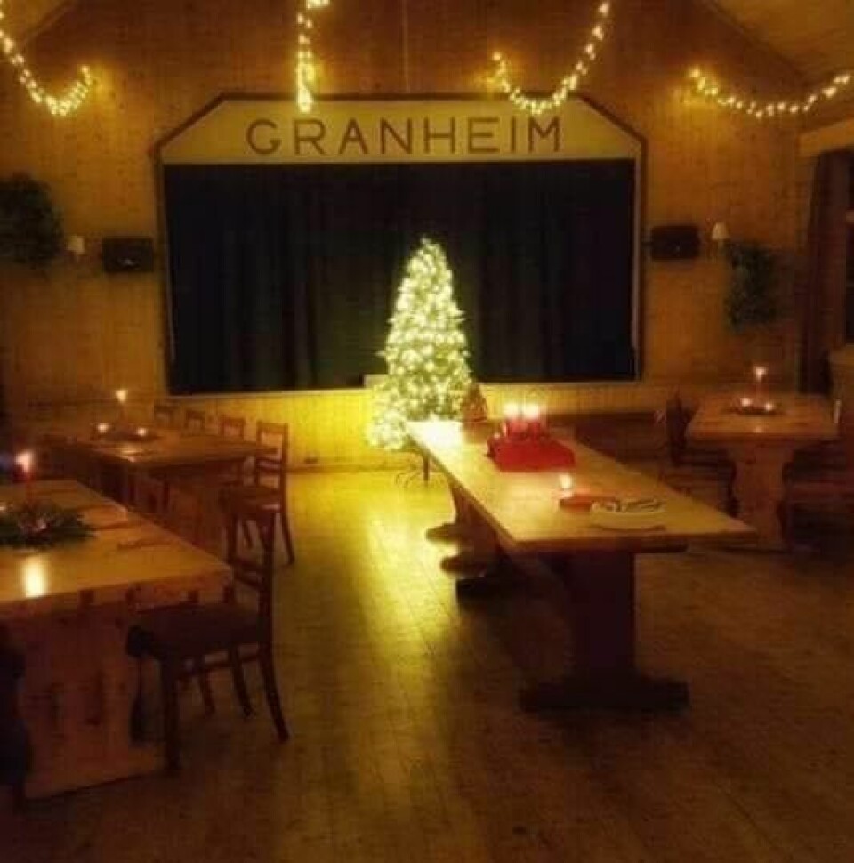 Et juletre står foran en scene. Over scenen står det 'Granheim'. Foran scenen er bord med levende lys