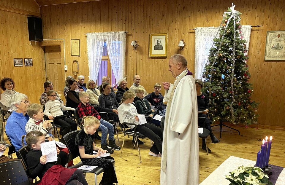 En prest som står foran en forsamling i et julepyntet forsamlingshus.