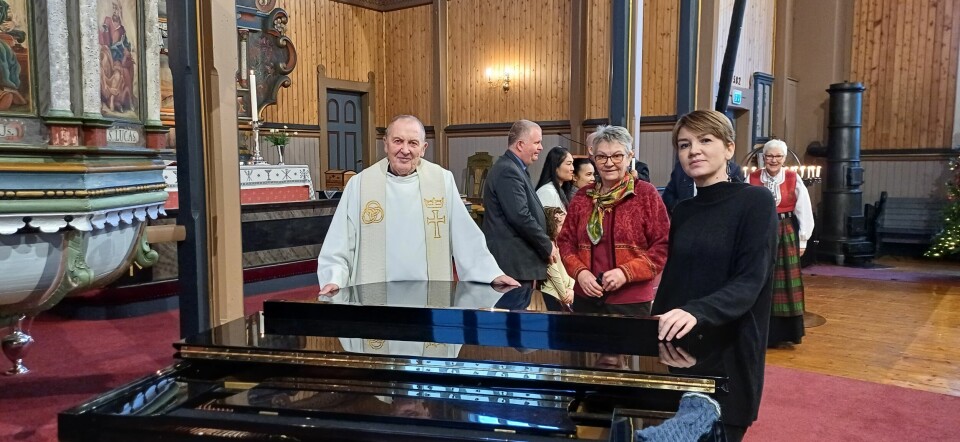 En prest og to kvinner står ved et piano.