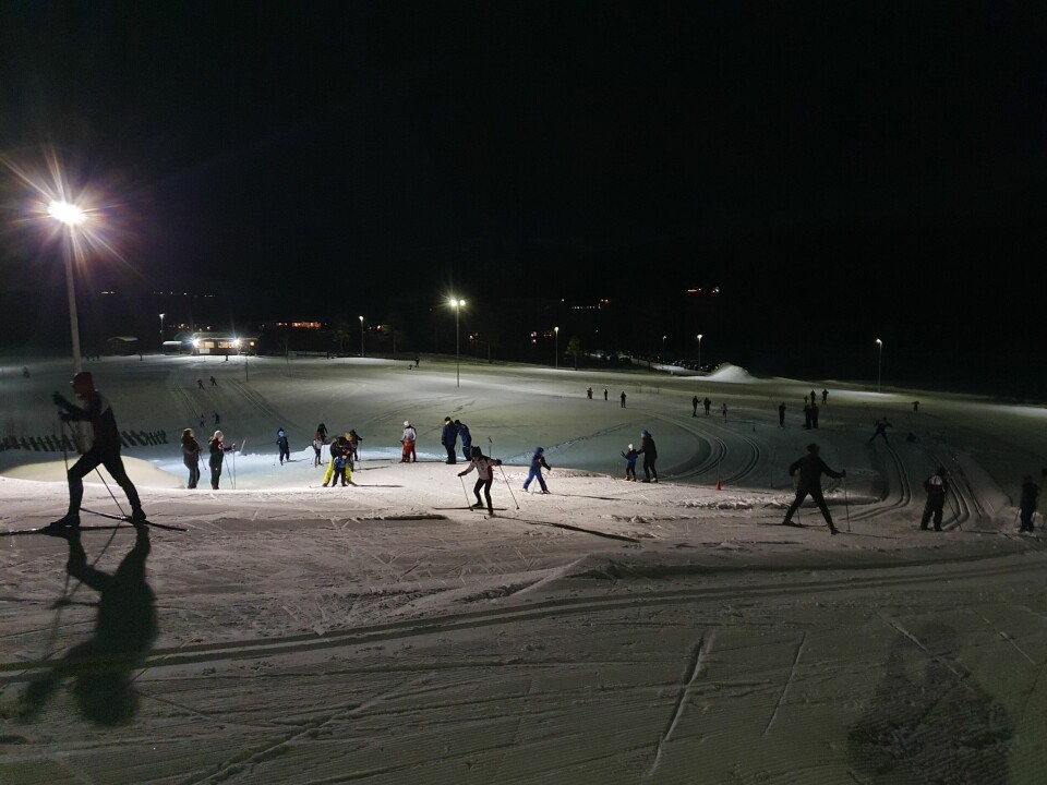 Mange mennesker går på ski på en skiarena i mørket