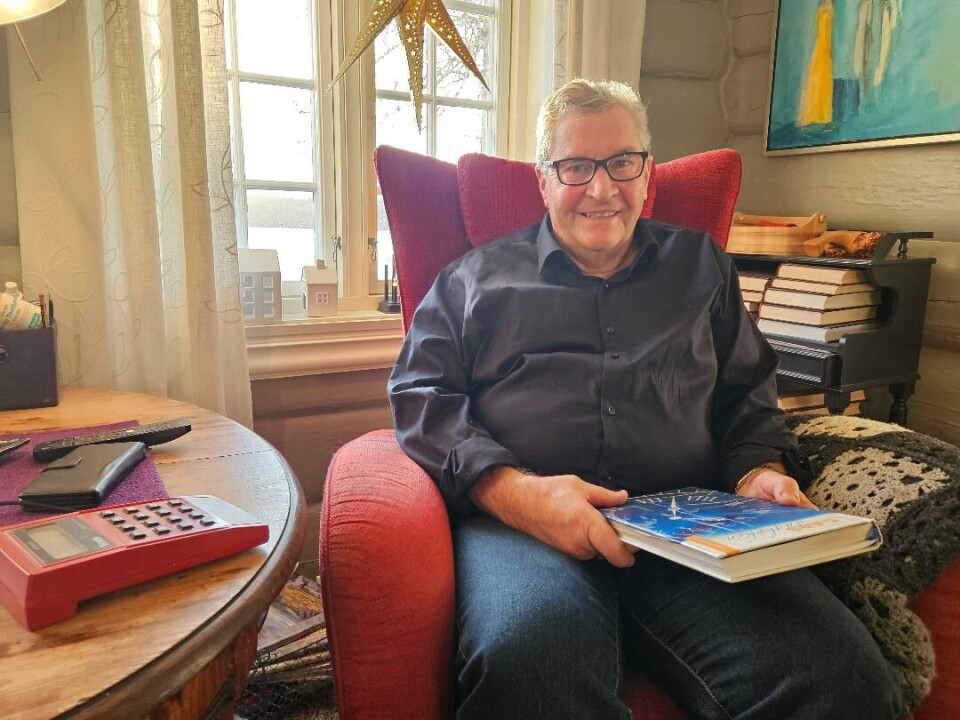 Magne i godstolen med dagboka og en av tidtakerklokkene sine. Mann i en stol. Mannen holder en bok.