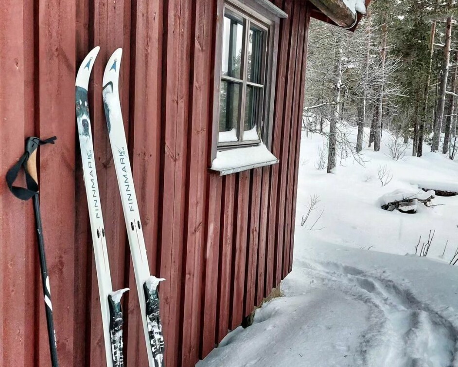 Ski og staver som står let opp mot en hyttevegg.