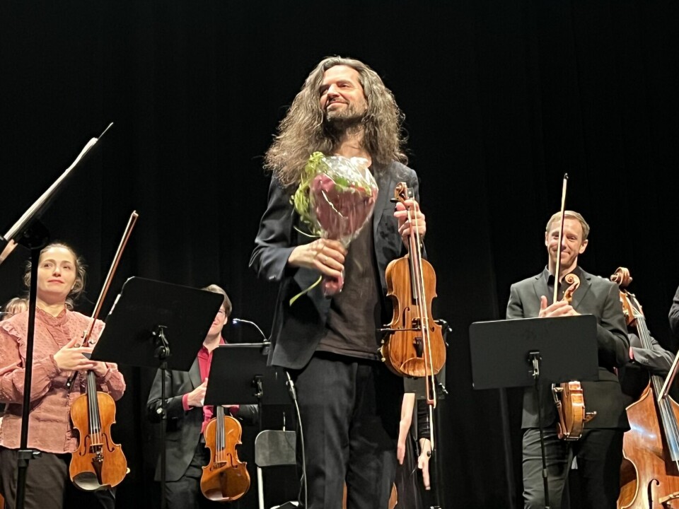 mann med blomster og fiolin på scene foran orkester