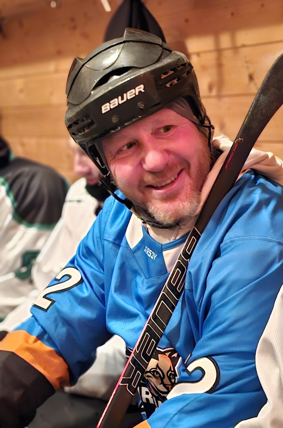 Mann i blå skjorte med nummertrykk og med skjegg i hvilebua i pausen med hjelm på hodet og hockeykølla i fanget