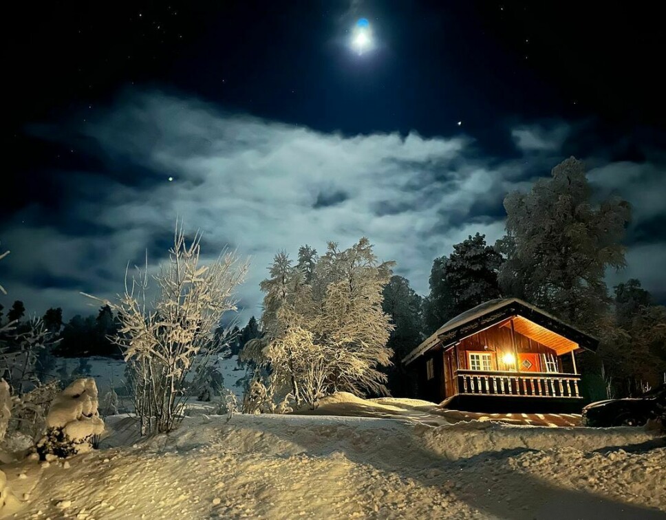 Ei hytte i snødekt skog. Månen lyser på nattehimmelen.