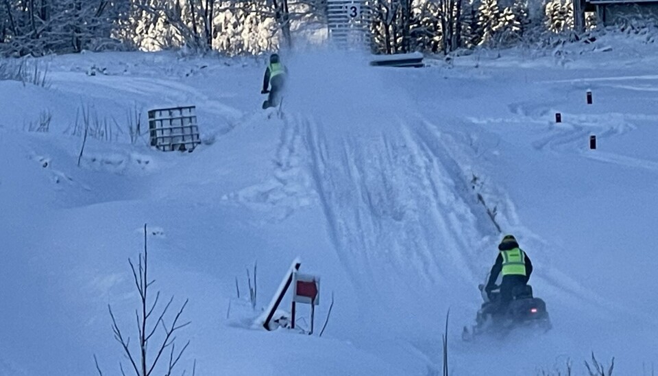 To snøscootere kjører opp en bakke. Godt vær og ren snø