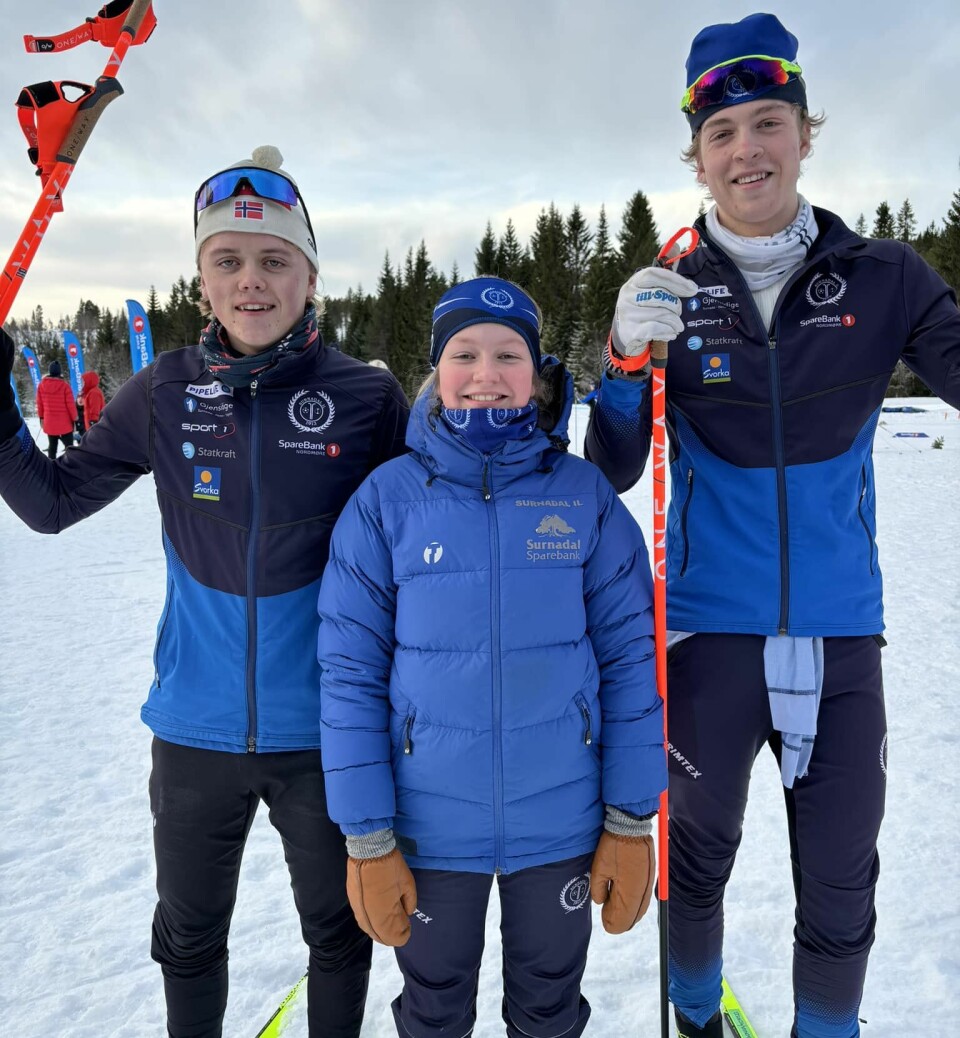 To unge gutter og en ung jente står med skiutstyr og smiler mot kamera