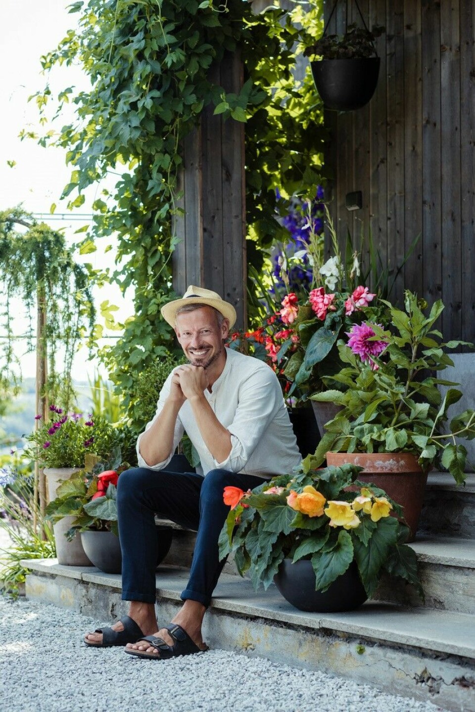 En mann sitter med mange blomster rundt seg