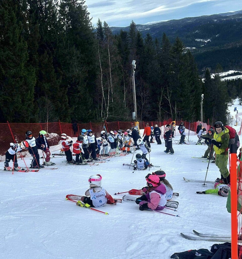 Mange barn med slalåmski og startnummer på brystet, på toppen av en liten alpinbakke.