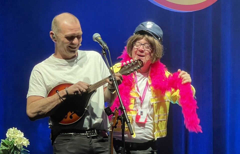 En mann spiller ukulele og en er ikledd rosa skjerf, hjelm og gul jakke.