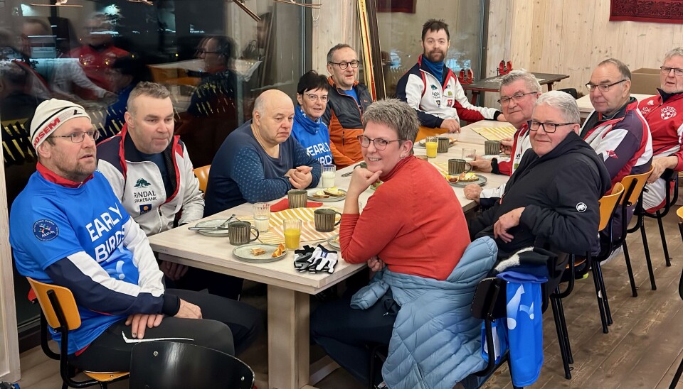 11 voksne personer sitter rund et langbord med frokosttallerken og kaffekopper.