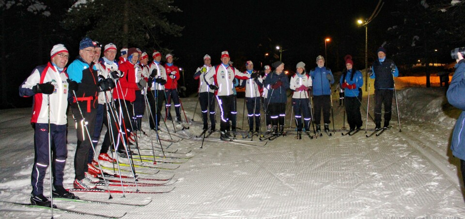 Omtrent 20 skiløpere oppstilt midt i lysløypa for fotografering, kan så vidt skimte fotografen til høyre.