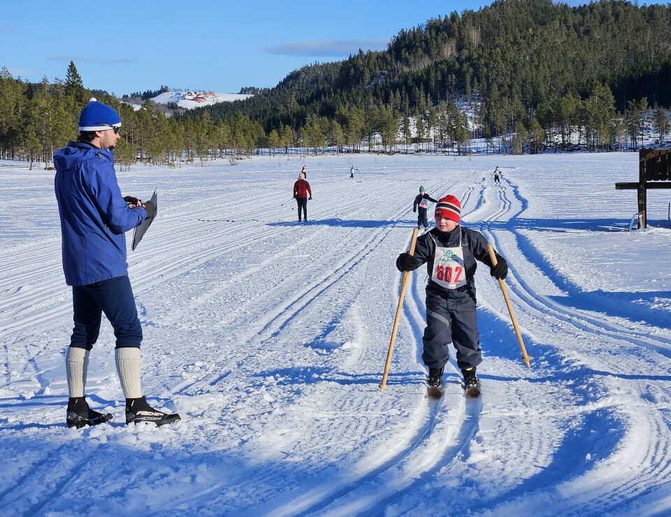 Barn på ski, med gammeldagse skistaver av tre. Tidtaker ved siden av