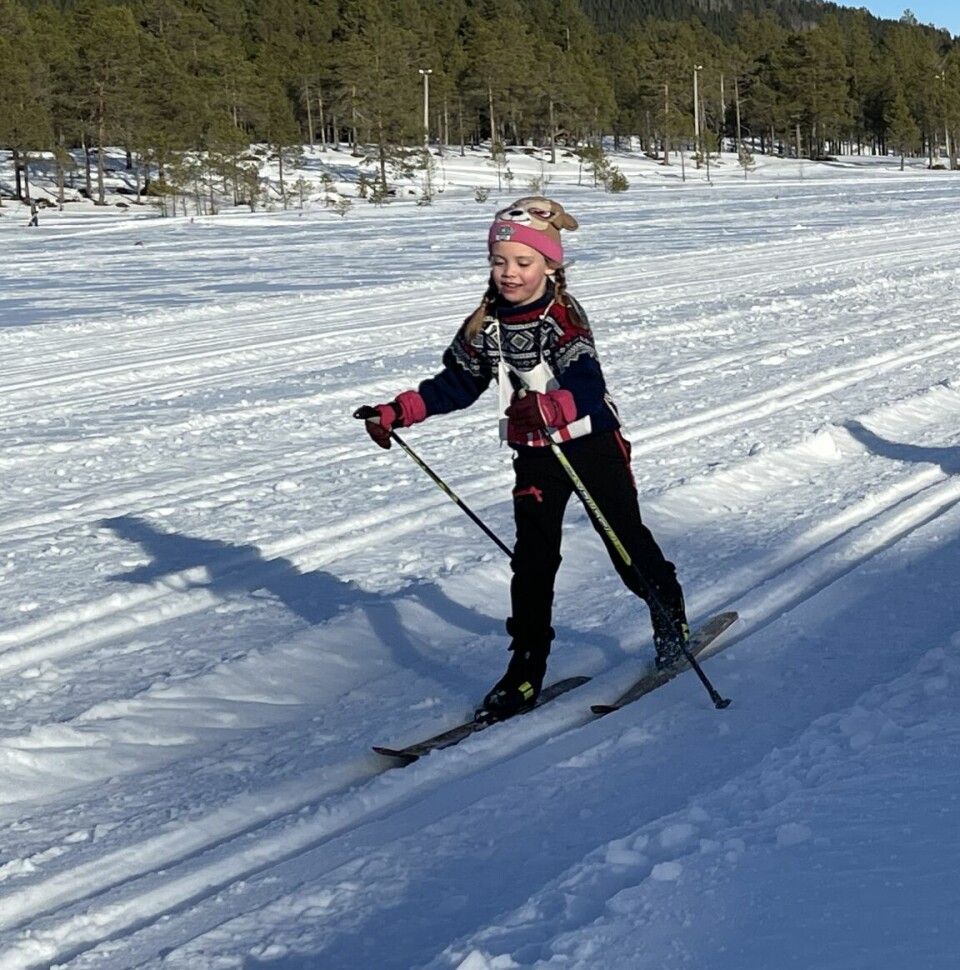 Et barn som går på ski. Et annet barn står ved siden av løypa