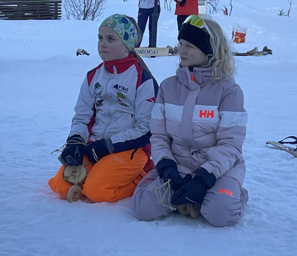 To vinterkledde jenter sitter på kne i snøen