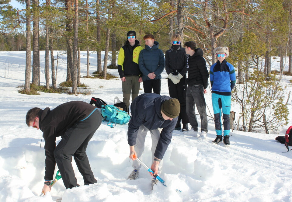 Elever graver i snøen mens noen andre ser på