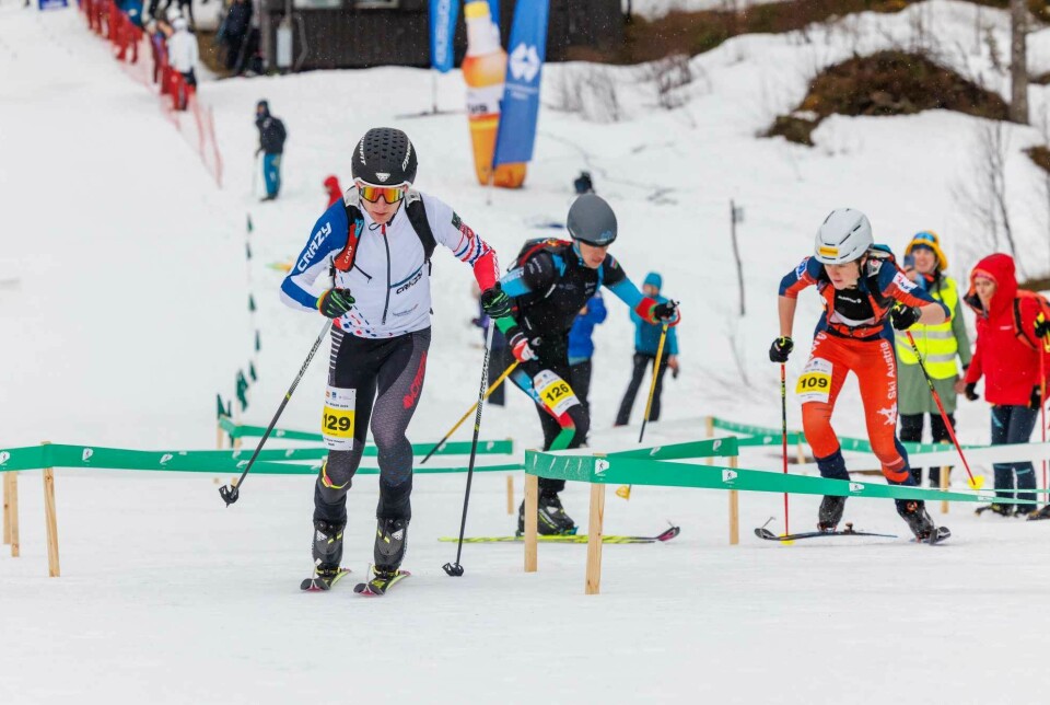 Flere unge menn med skiutstyr, hjelm og startnr, som konkurrerer.