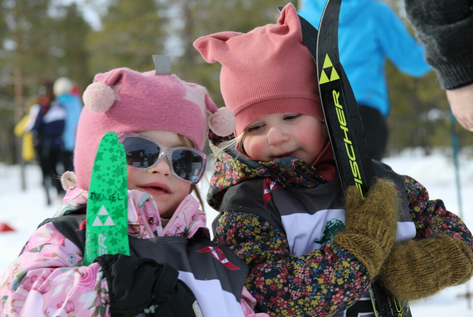 nærbilde av to jenter i fargerike vinterdresser og rosa luer holder opp skia sine for fotografen.