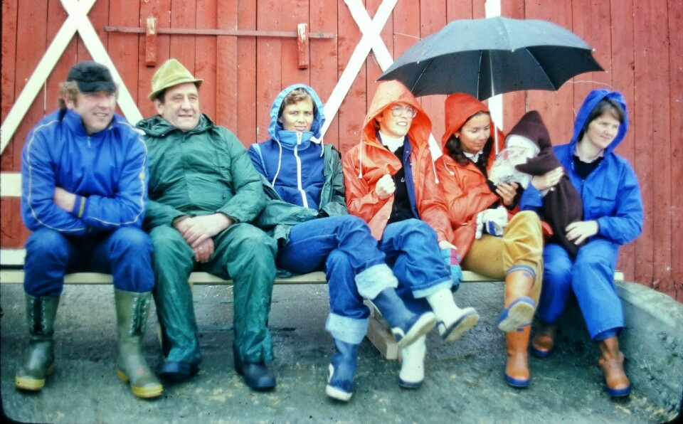 De voksne sitter på en benk på låvebrua og ser på premieutdeling. De fleste har regntøy og støvler.