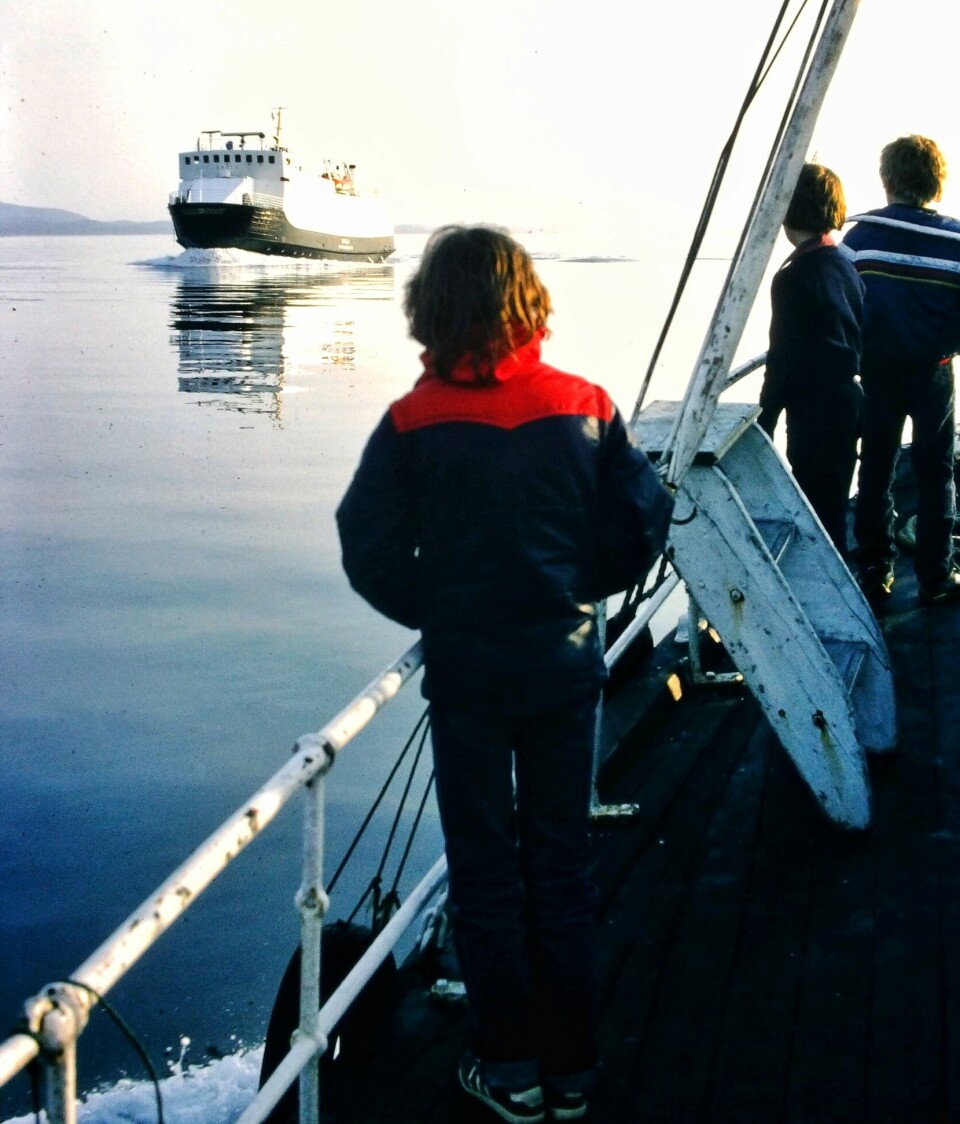 Bilde er tatt ved rekka på båten. 3 barn ser på ferja som kommer i mot.