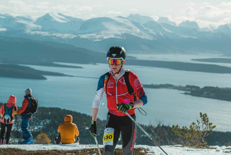 En ung mann som går i en skikonkurranse. Fjord og fjell i bakgrunnen.