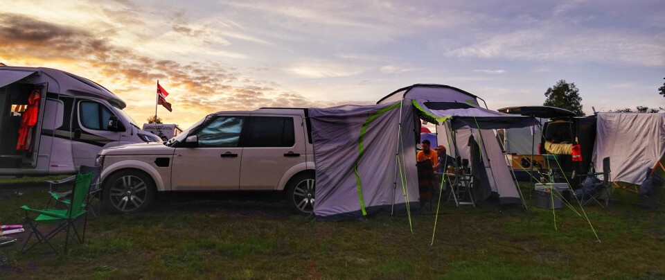 En hvit Landrover i solnedgang med telt festet til bakluka på bilen.