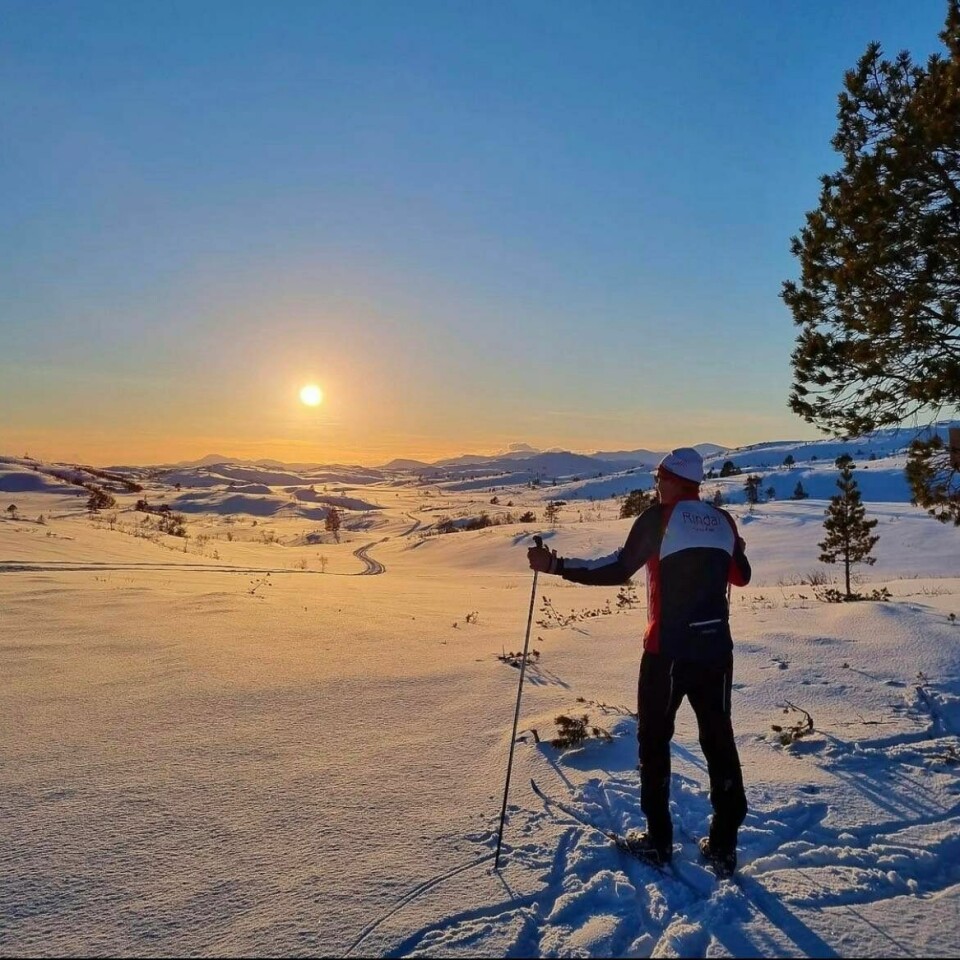 En mann på ski som står og ser på solnedgangen.