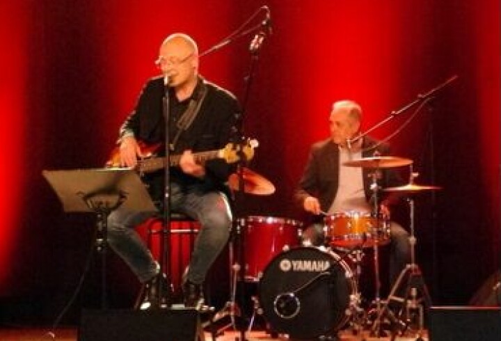 En mann med gitar og en med trommer på en scene.