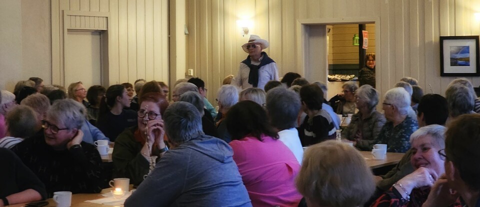Mann i lys hatt og skjorte, med mørk genser over skuldrene går mellom bordene i salen.