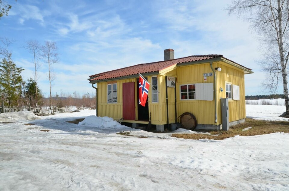 Et lite gult hus med et norsk flagg utenfor.
