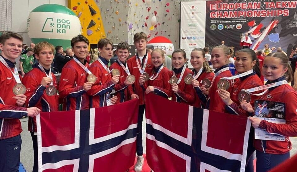 Man landslagskledde ungdommer med et norsk flagg foran seg.