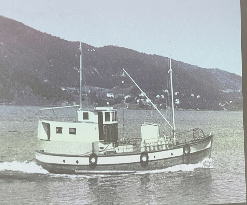 En trebåt på veil ut en fjord. Hus i bakgrunnen