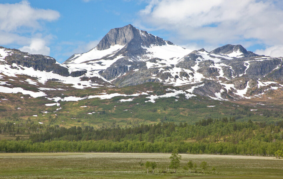 Et fjell med litt snø og grønt gress på bakken