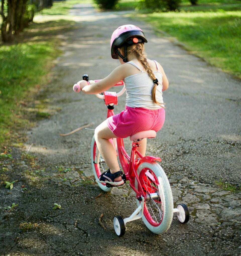 Et barn på sykkel med støttehjul, og sykkelhjelm på hodet.