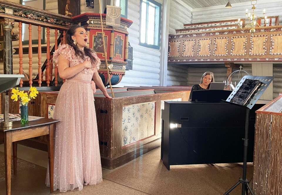 Ei dame som står og synger i ei kirke. I bakgrunnen ei dame som spiller piano.